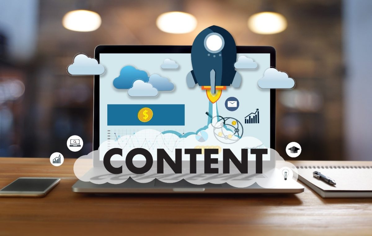 Laptop on a desk with 3D figures coming out such as a rocket ship, clouds and the word "Content."